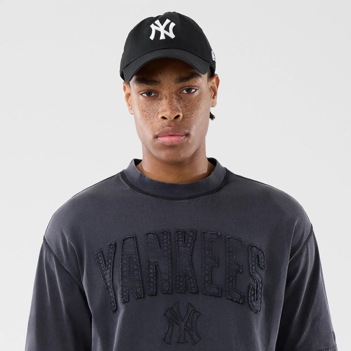 New Era New York Yankees MLB Washed Black T-Shirt, front view on-model with matching black cap, featuring large Yankees lettering across the chest and the NY logo embossed below, both in black on the washed fabric.