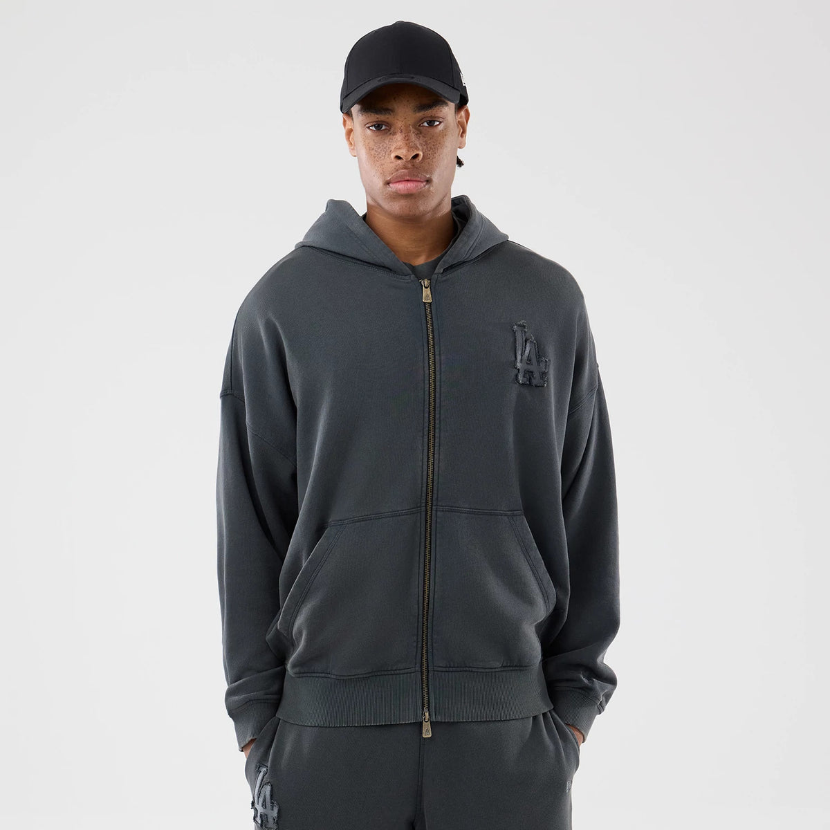 New Era LA Dodgers MLB Washed Dark Grey Full Zip Hoodie, front view showing the dark grey zip closure down the centre, raised LA logo on the left chest, on-model with a plain black cap worn for styling.
