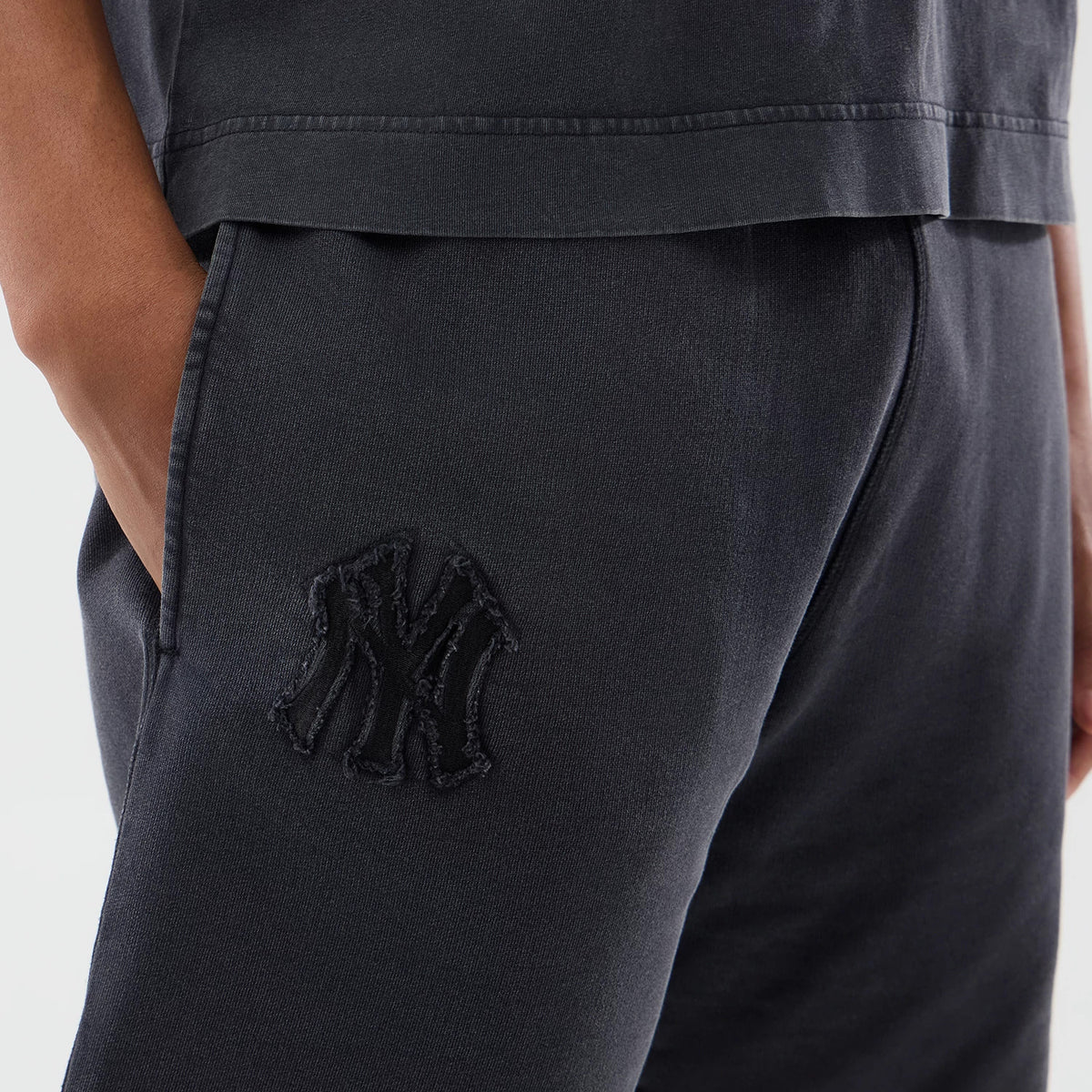 New Era New York Yankees MLB Washed Black Shorts, three-quarter view showing the black shorts with one hand in the pocket and a large raised New York Yankees logo on the lower left leg.