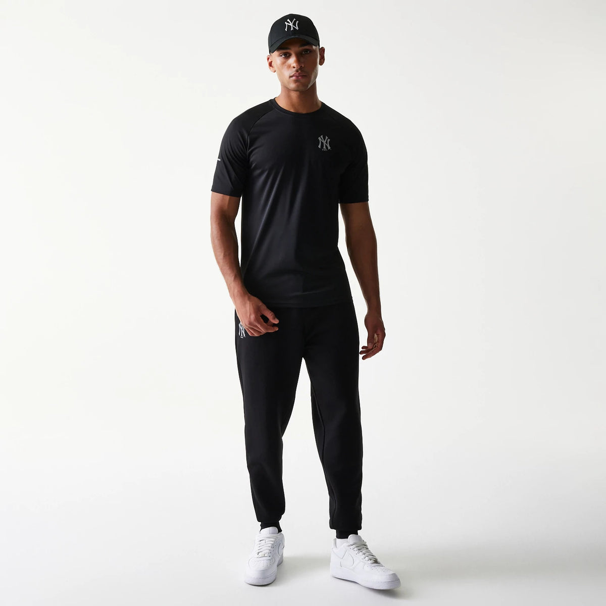 New Era New York Yankees MLB Reflective Black T-Shirt, front view on-model showcasing the reflective Yankees logo embroidered on the left chest and short sleeves, paired with matching black joggers and a Yankees cap.