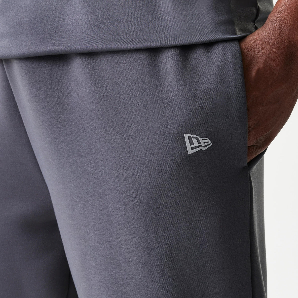 New Era New York Yankees MLB Dark Grey Joggers, close-up showing the New Era flag logo embroidered in light grey on the upper left thigh, with a pocket detail and dark grey fabric texture.
