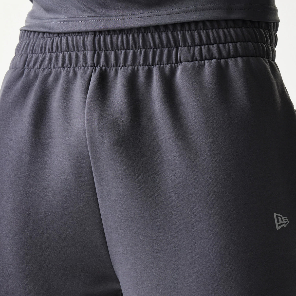 New Era New York Yankees MLB Dark Grey Joggers, close-up view showing the elasticated waistband and the New Era flag logo on the left hip, highlighting the dark grey fabric and casual fit.