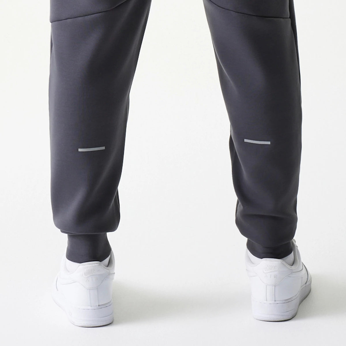 New Era New York Yankees MLB Dark Grey Joggers, rear view showing reflective strip on the lower legs of the dark grey fabric, with elasticated cuffs and paired with white trainers.