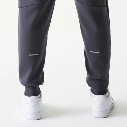 New Era New York Yankees MLB Dark Grey Joggers, rear view showing reflective strip on the lower legs of the dark grey fabric, with elasticated cuffs and paired with white trainers.