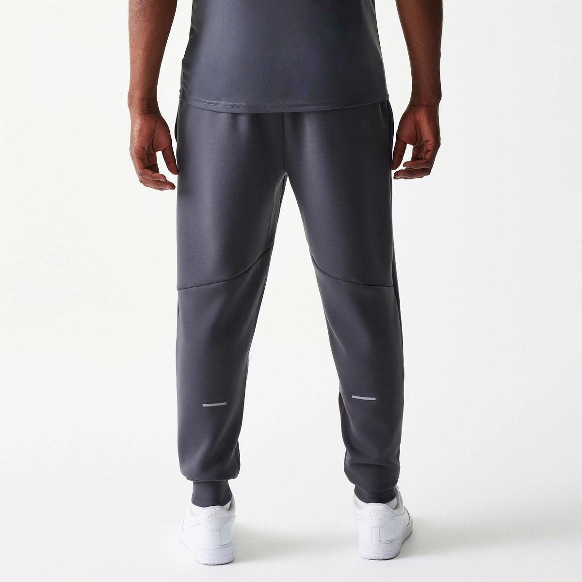 New Era New York Yankees MLB Dark Grey Joggers, back view on model showing the tapered fit with elasticated cuffs at the ankles, seam details across the knees, and a dark grey finish paired with white trainers.