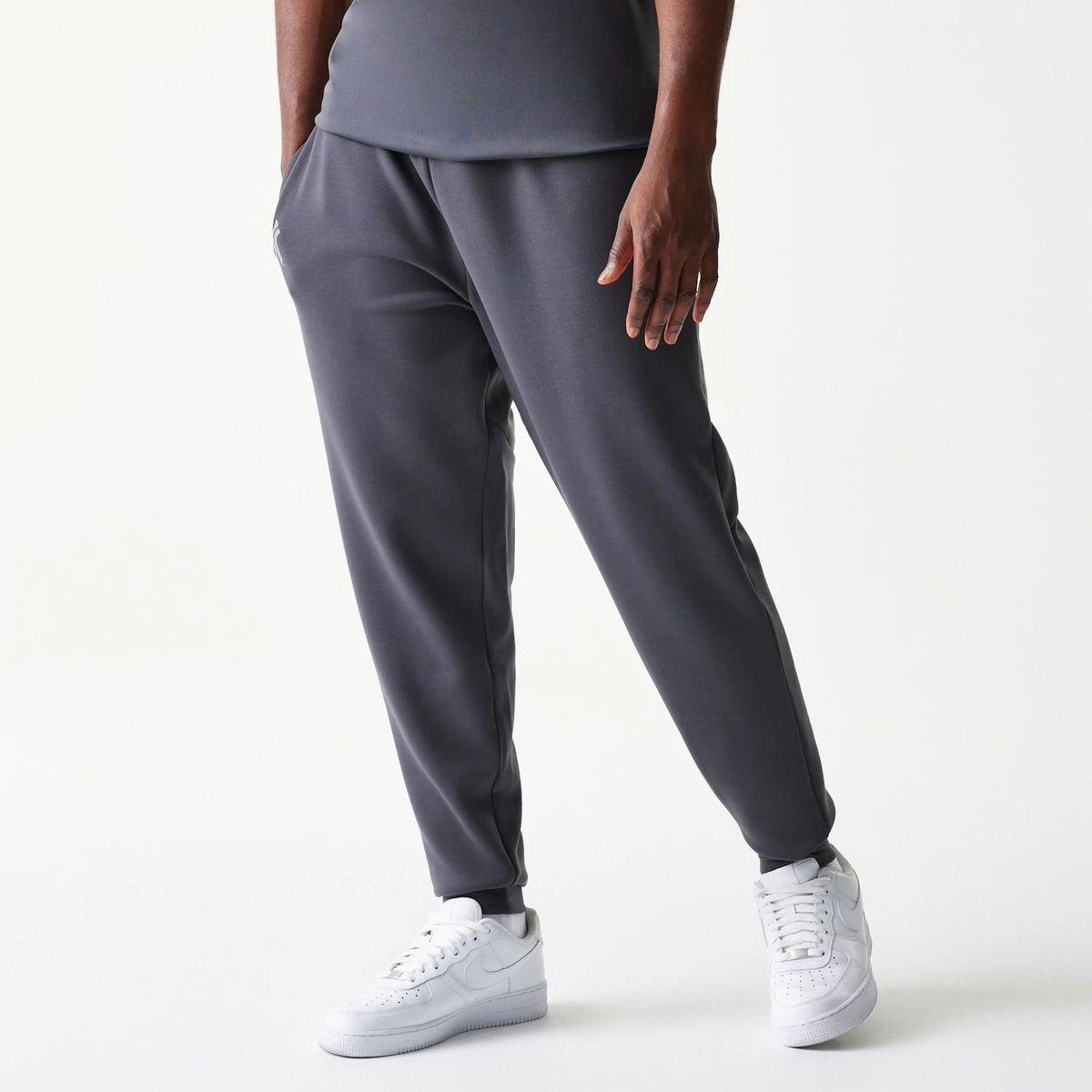 New Era New York Yankees MLB Dark Grey Joggers, front view showing a relaxed fit with side pockets and an embroidered white New Era logo below the left pocket, styled with white trainers for a casual look.