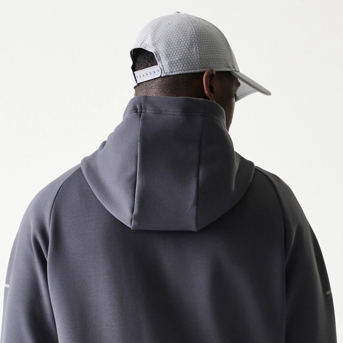 New Era New York Yankees MLB Dark Grey Full Zip Hoodie, back view highlighting the attached hood and dark grey finish, worn on a model paired with a light grey New Era cap displaying a pattern.