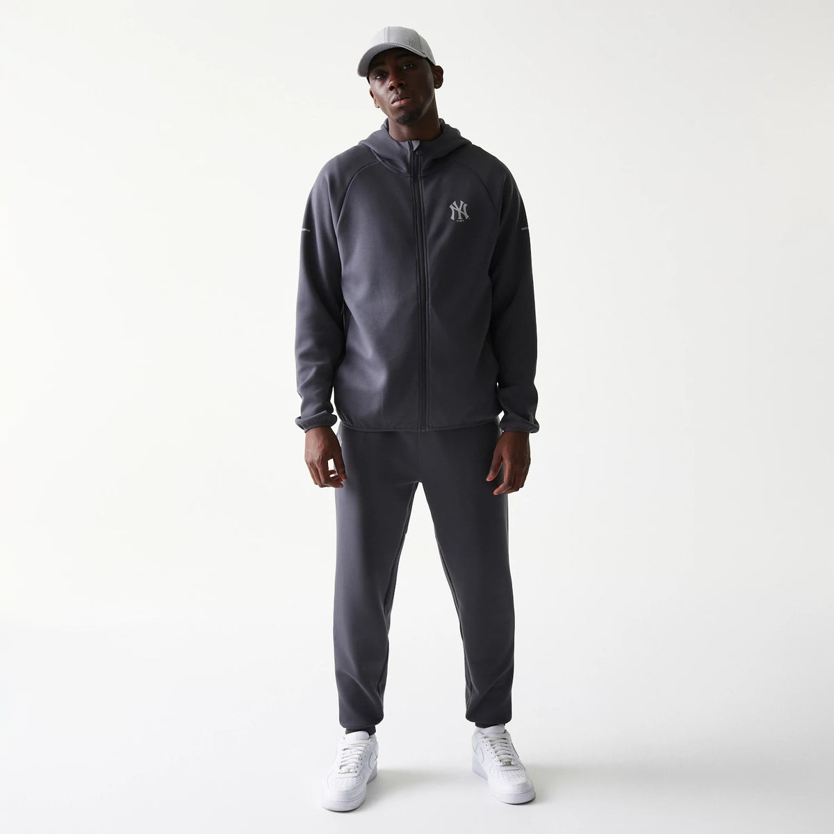 New Era New York Yankees MLB Dark Grey Full Zip Hoodie, front view on-model with matching dark grey joggers and a light grey cap, featuring an embroidered Yankees logo on the left chest and a full-length zip running down the centre.