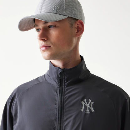 New Era New York Yankees MLB Dark Grey Jacket, three-quarter view on a model showing a raised Yankees logo on the left chest, a high collar with a centred zip, styled with a grey cap featuring an embossed logo on the crown.