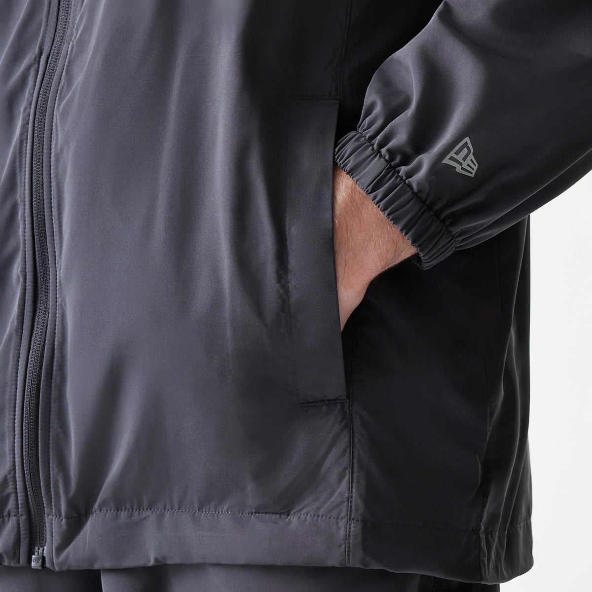 New Era New York Yankees MLB Dark Grey Jacket, side view showing a zip closure along the front, an elasticated cuff with an embroidered New Era logo on the sleeve, and a hand casually slipped into the side pocket.