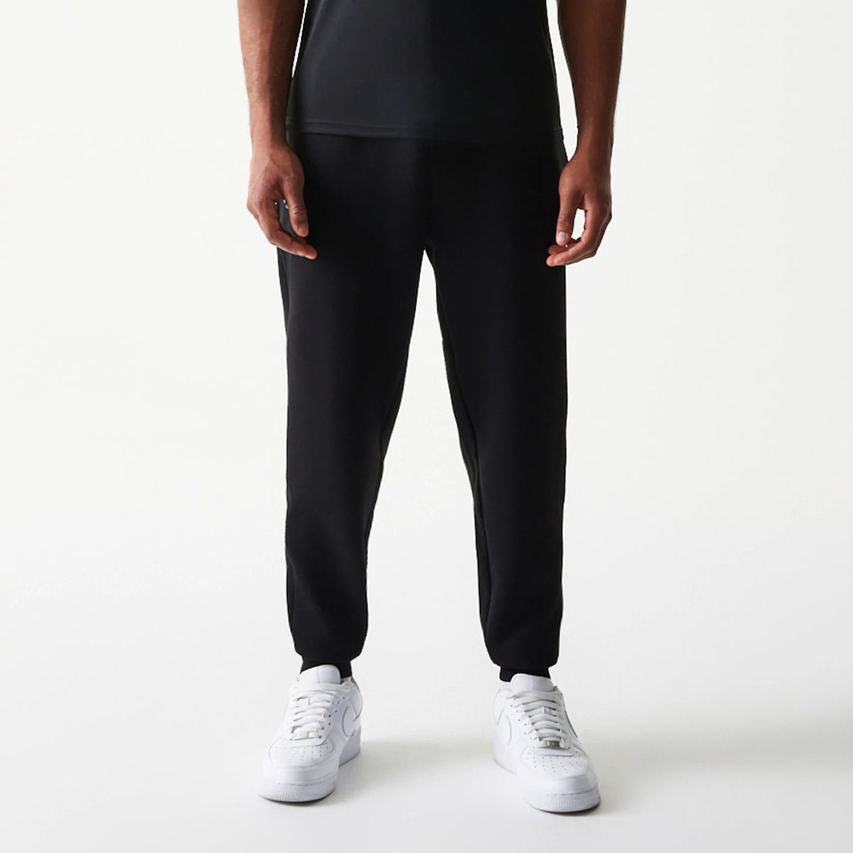 New Era New York Yankees MLB Black Joggers, front view on a model wearing white trainers, showing the relaxed fit through the legs and elasticated cuffs for a tapered look in solid black fabric.
