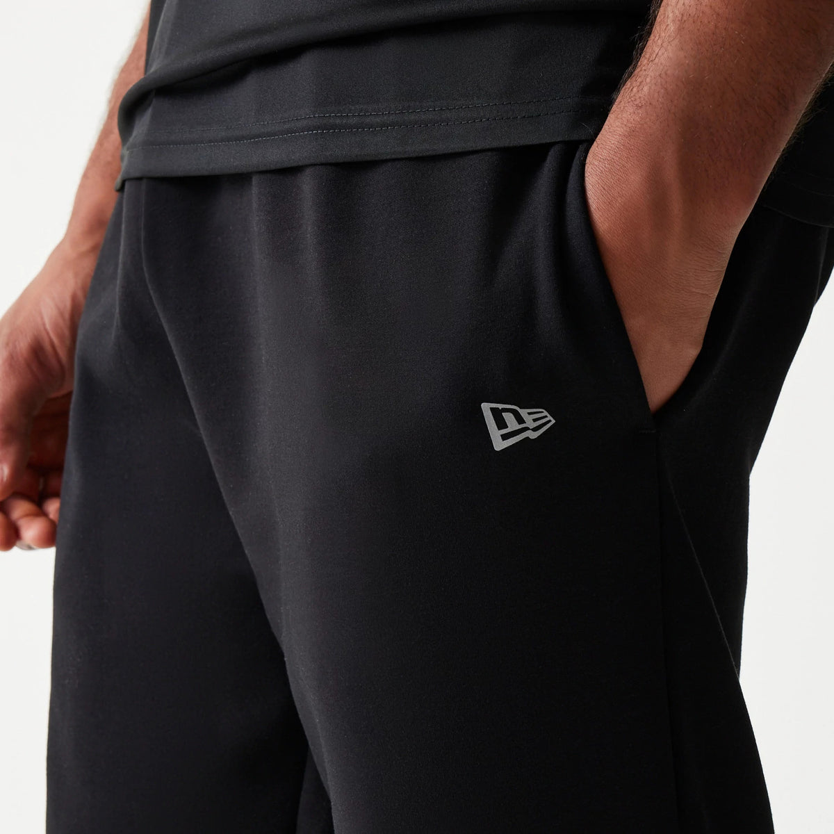 New Era New York Yankees MLB Black Joggers, side view with a model showing the grey New Era flag logo on the lower left leg, featuring an elasticated waistband and side pockets in a soft fabric finish.