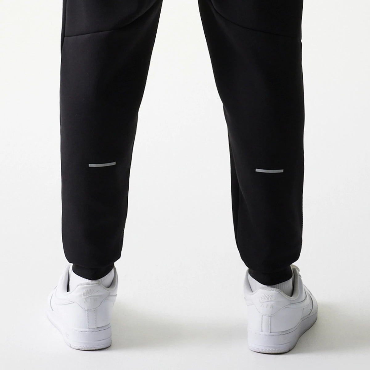 New Era New York Yankees MLB Black Joggers, rear view on a model showing reflective stripes on the lower legs, with elasticated cuffs and paired with white trainers, emphasising a casual athletic style.