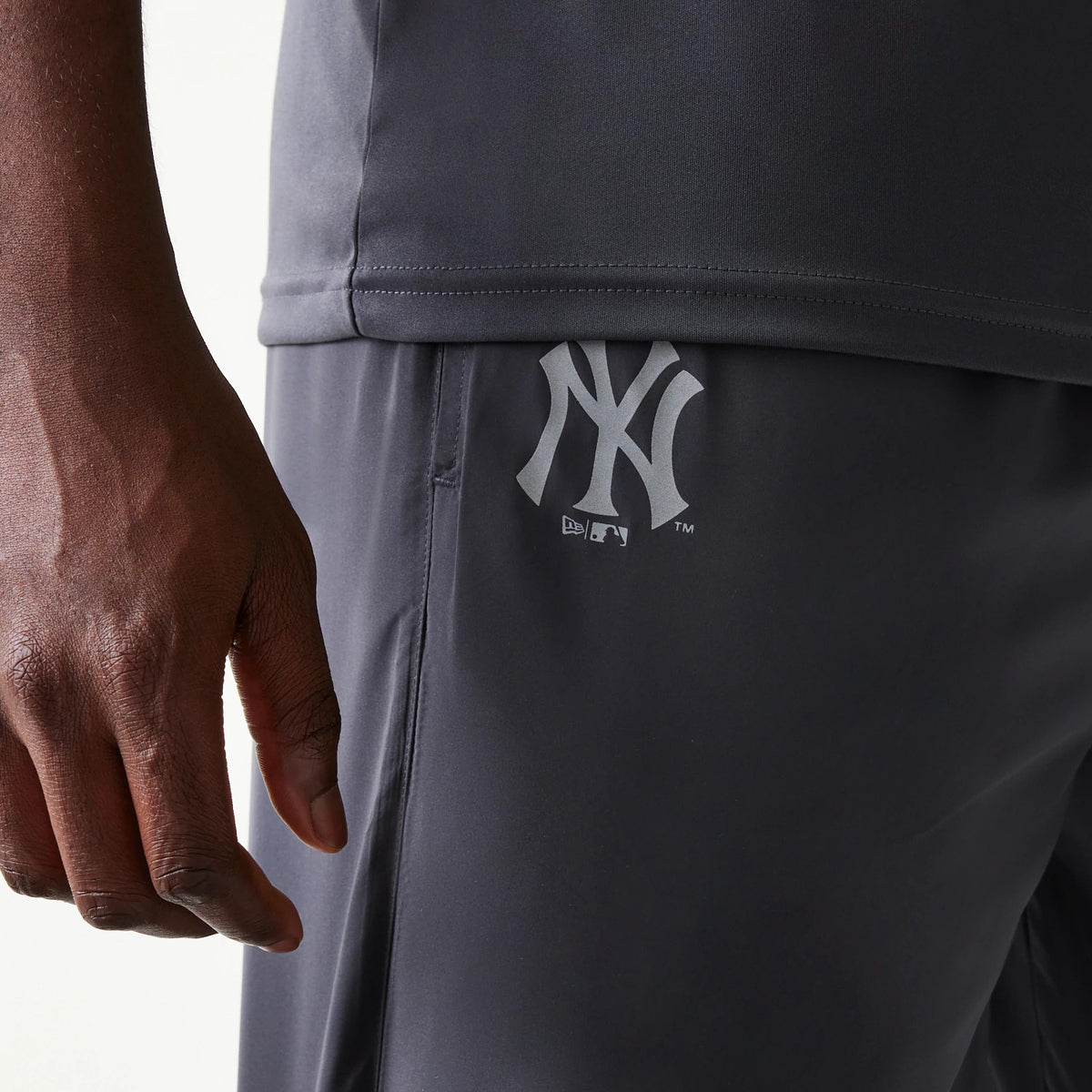 New Era New York Yankees MLB Dark Grey Track Pants, side view showing the light grey Yankees logo printed on the upper left leg of the dark grey fabric, with a relaxed fit and elastic waistband.