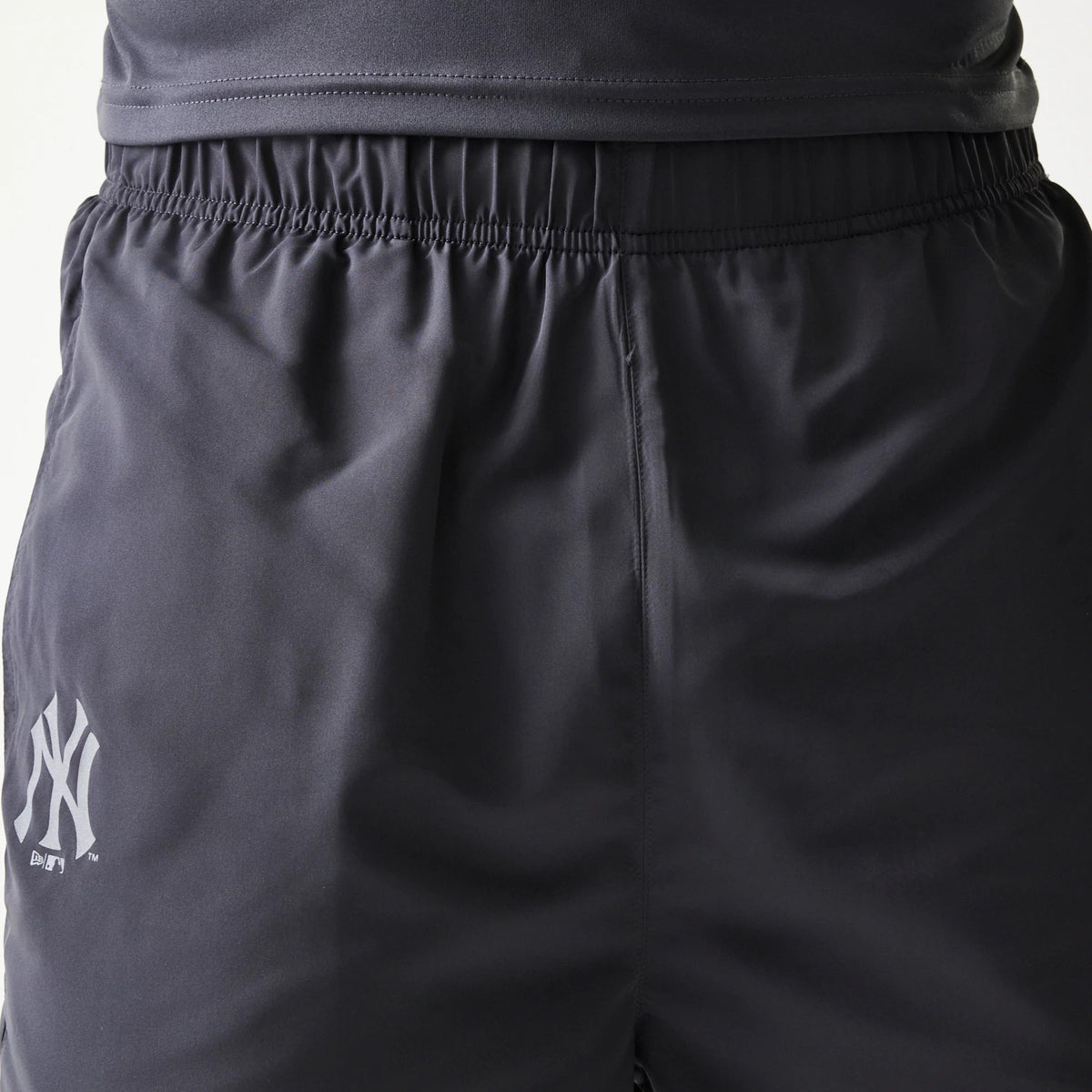 New Era New York Yankees MLB Dark Grey Track Pants, close-up showing the elastic waistband and silver NY logo embroidered on the left thigh, with fabric for a and comfortable fit.