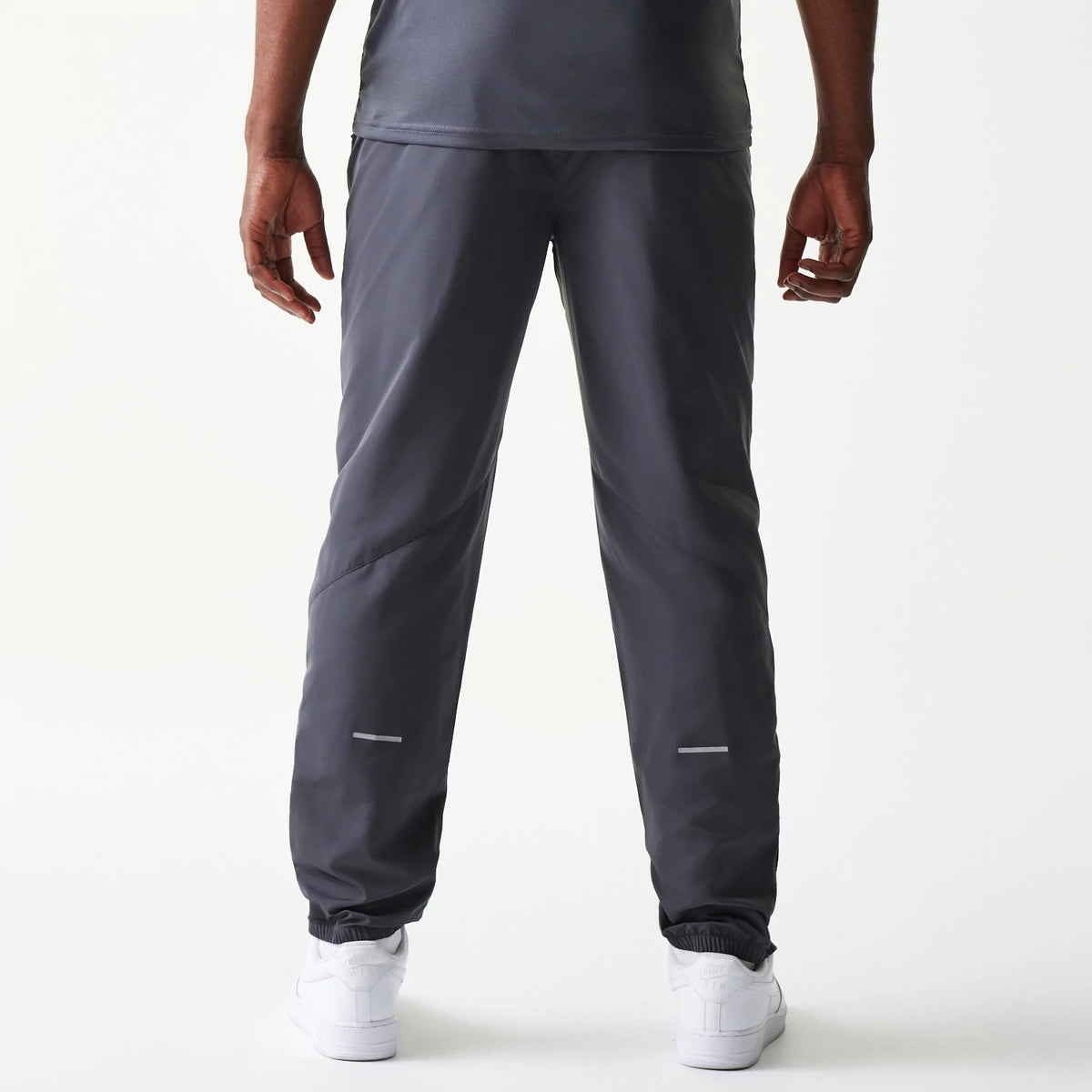 New Era New York Yankees MLB Dark Grey Track Pants, rear view showing a straight-leg cut with elasticated cuffs and reflective near the ankles, styled over white trainers on a model.
