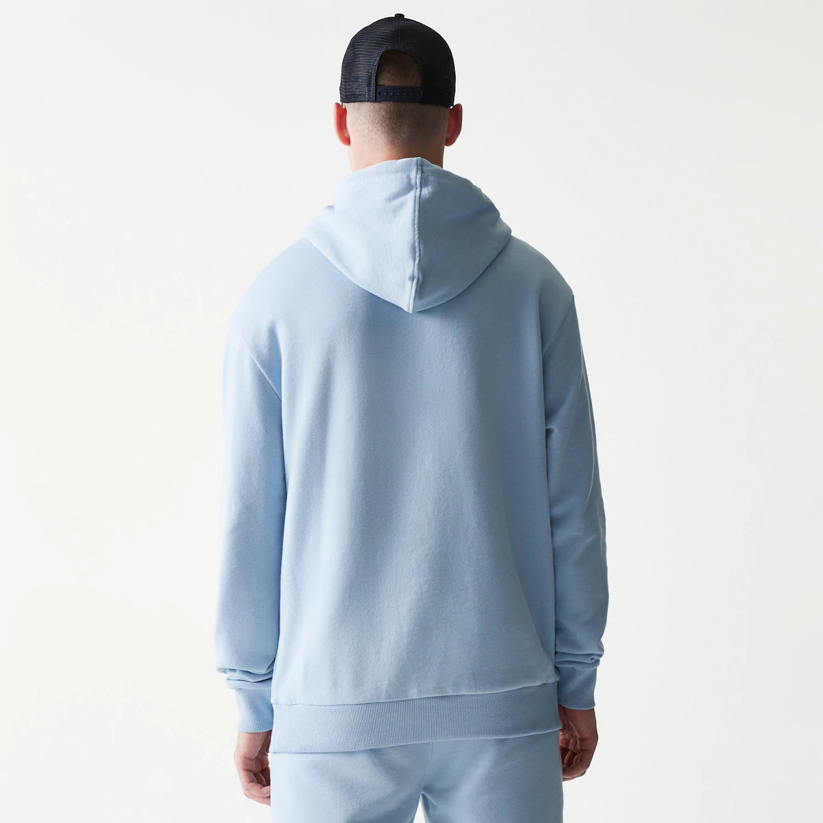 New Era New York Yankees MLB Midi Pastel Blue Oversized Pullover Hoodie, back view on a model pairing it with matching joggers and a black cap, showing the simple pastel blue design with a roomy hood and long sleeves.
