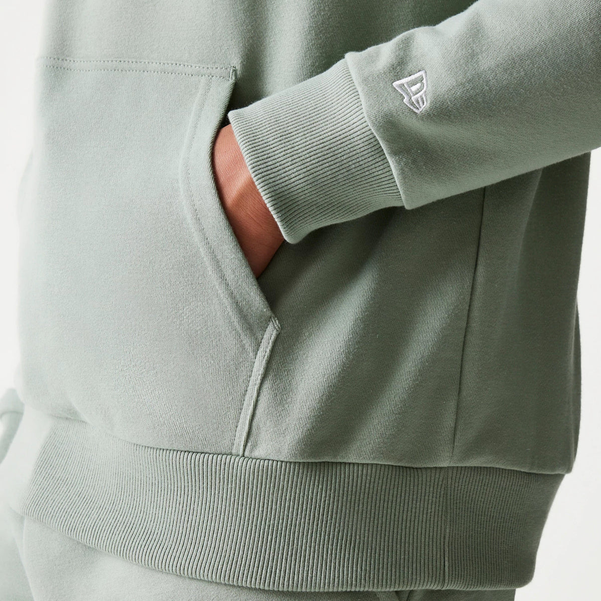 New Era LA Dodgers MLB Midi Green Oversized Pullover Hoodie, detailed view showing the light green fabric with a ribbed cuff and waistband, hand placed in the front pouch pocket, and a small embroidered New Era logo on the sleeve.