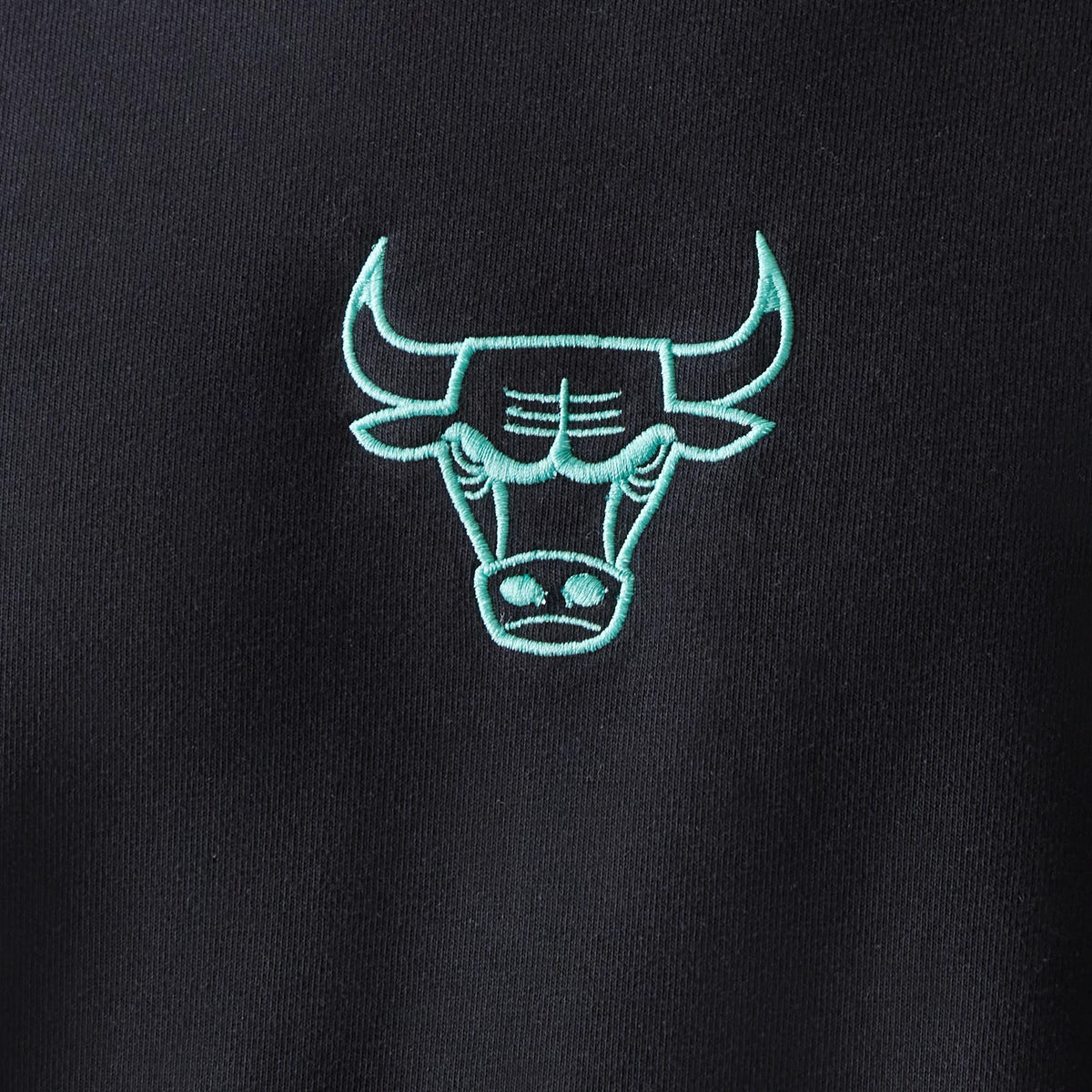 New Era Chicago Bulls NBA Black Oversized Crew Neck Sweater, close-up showing a mint green embroidered Bulls logo centred on the chest, set against a black fabric for contrast and style.