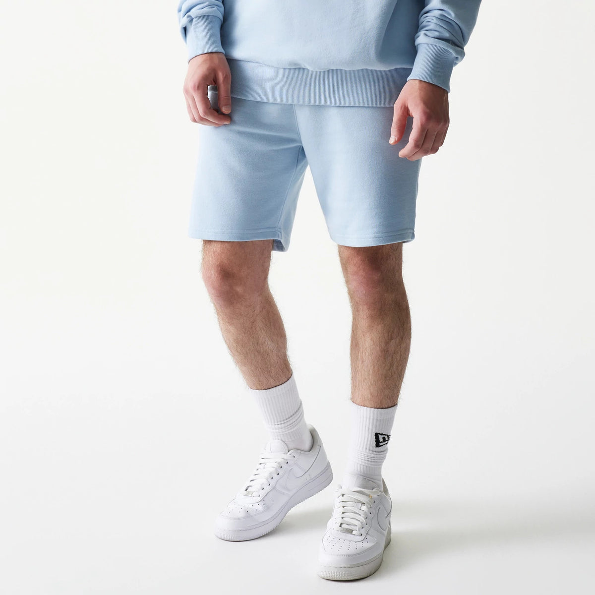 New Era New York Yankees MLB League Essential Midi Blue Shorts, front view on-model showing the light blue shorts paired with a matching sweatshirt, featuring a waistband and a small embroidered New Era logo on the socks.