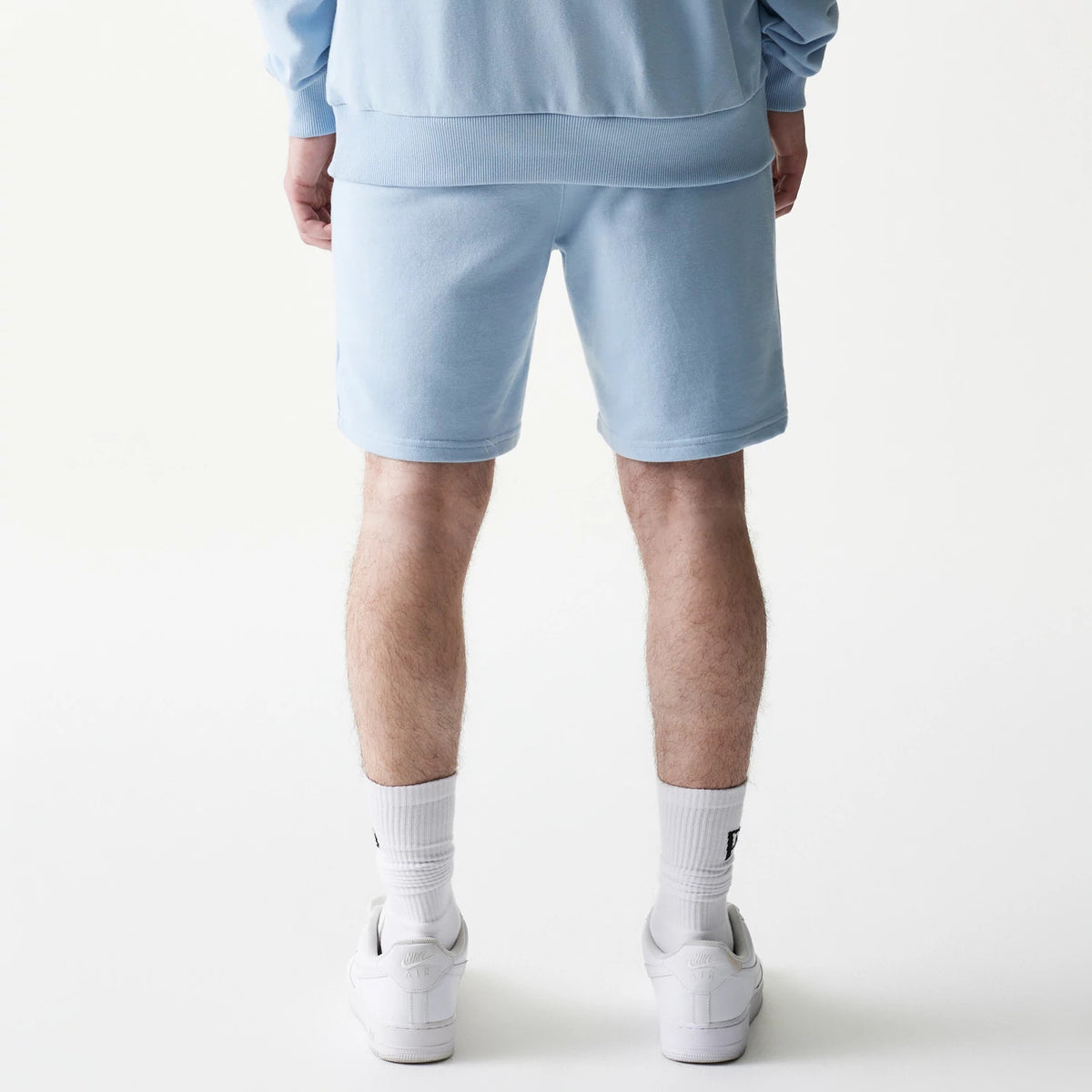 New Era New York Yankees MLB League Essential Midi Blue Shorts, back view on a model styled with a matching blue top, showing the solid light blue colour of the shorts and a fitted waistband.