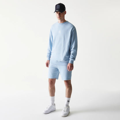 New Era New York Yankees MLB League Essential Midi Blue Shorts, on-model front view showing the shorts styled with a matching sweatshirt, embroidered Yankees logo on the left leg, and paired with white trainers and socks.