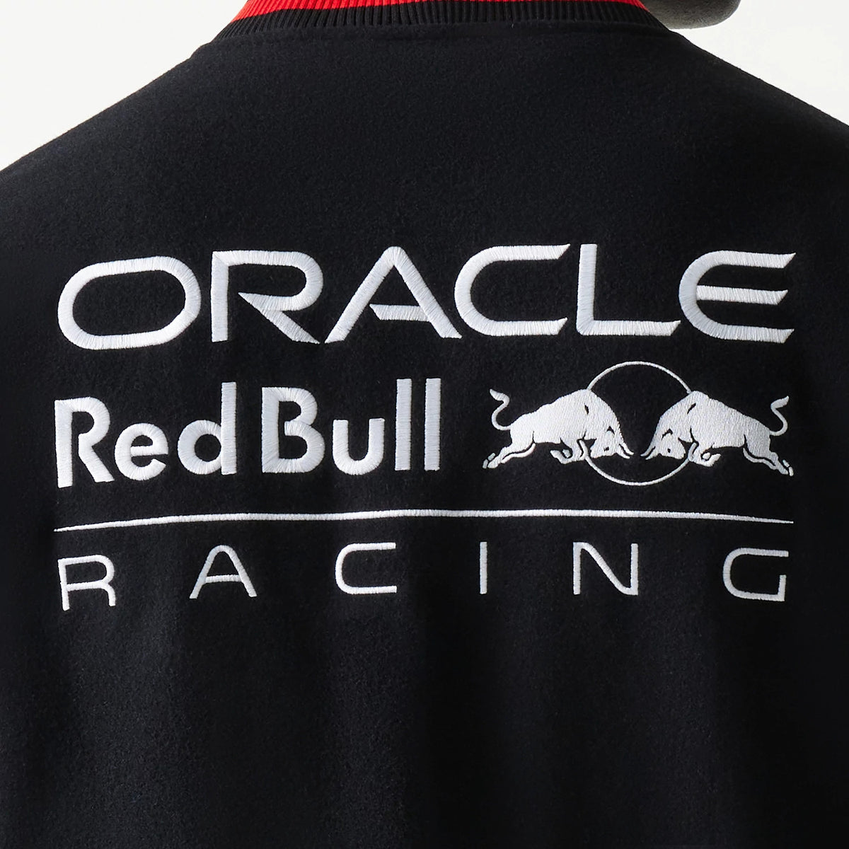 New Era Red Bull Racing Black Varsity Jacket, back view showing the large white embroidered lettering of Oracle and Red Bull Racing across the shoulders and upper back, accented by two charging bull graphics in the centre.