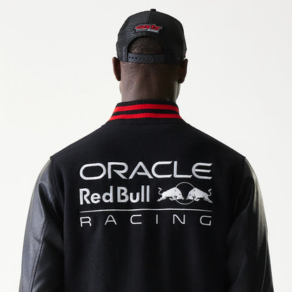 New Era Red Bull Racing Black Varsity Jacket, back view showing the large printed Oracle Red Bull Racing logo across the shoulders, with black sleeves and a red striped collar, worn by a model wearing a black cap.