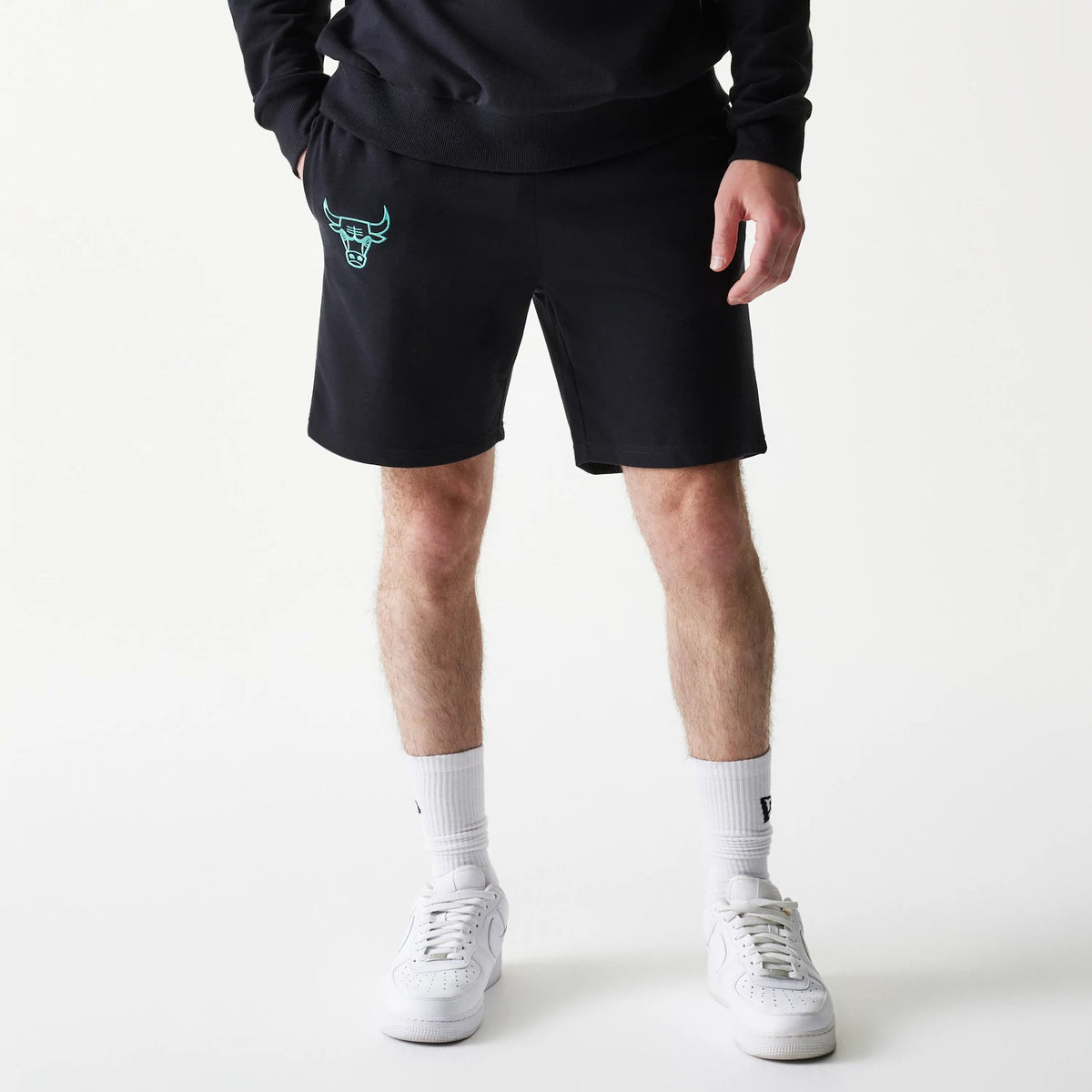 New Era Chicago Bulls NBA Core Black Shorts, front view displaying black shorts with an embroidered turquoise Chicago Bulls logo on the left leg, styled simply with white sneakers and socks.