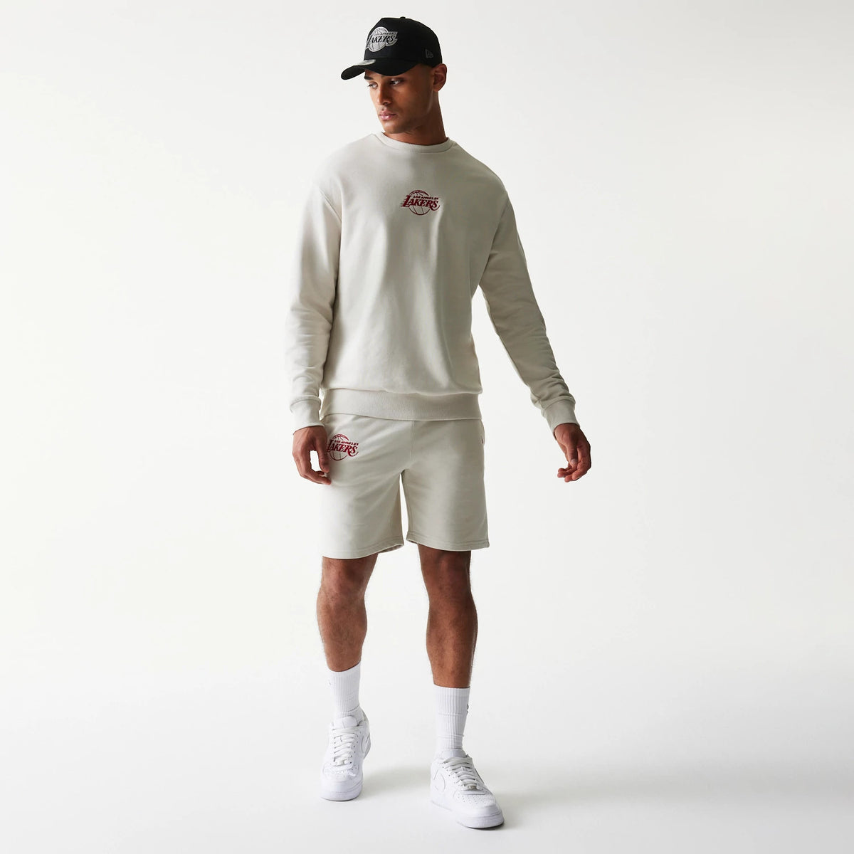 New Era LA Lakers NBA League Essential Light Beige Shorts, front view showing the embroidered Lakers logo on the left leg, styled with a light beige sweatshirt featuring a matching logo on the chest.