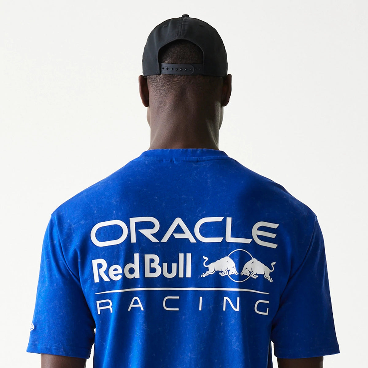 New Era Red Bull Racing Linear Graphic Blue Oversized T-Shirt, back view on a model showing large white Oracle Red Bull Racing lettering with graphic bulls printed across the upper back against a blue background.