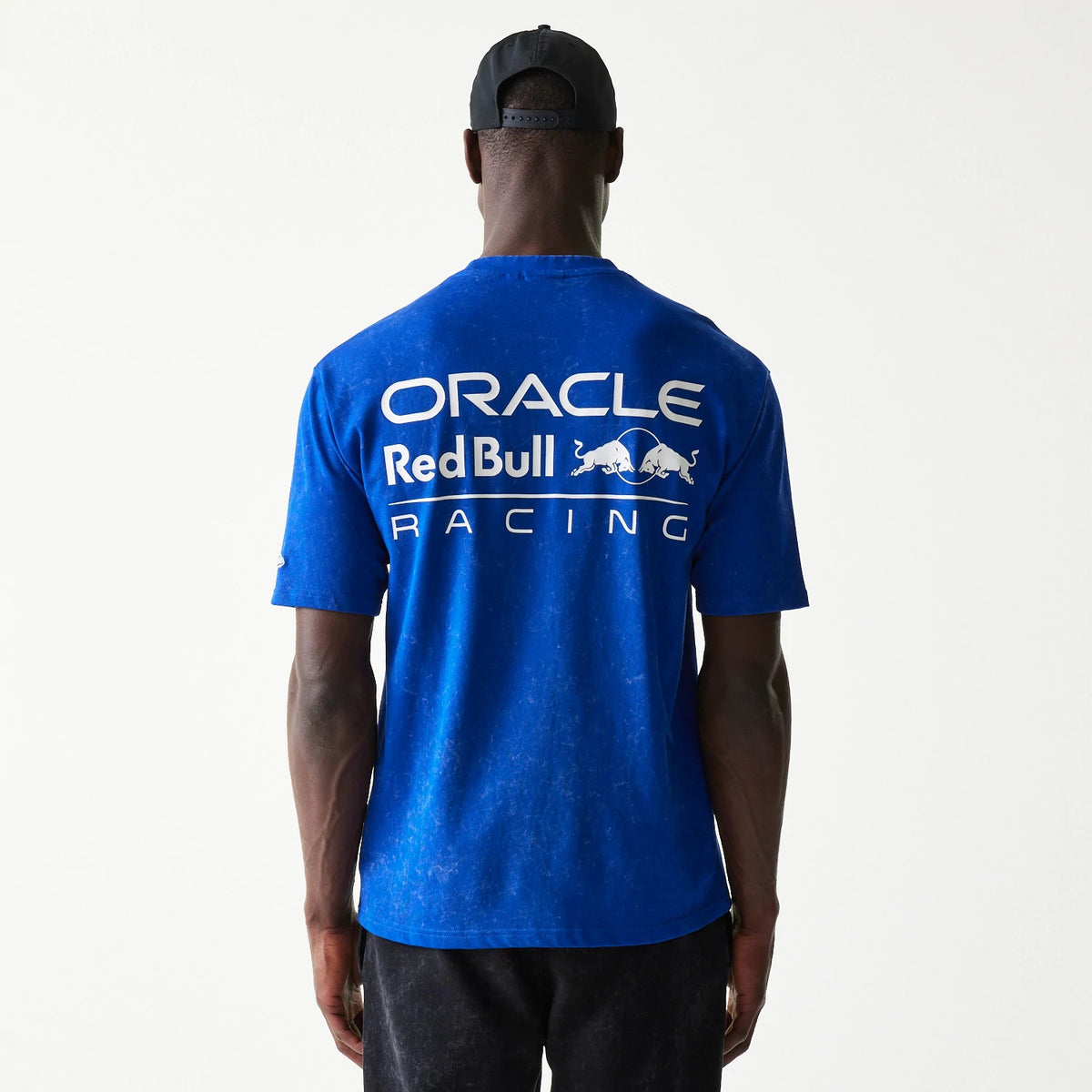 New Era Red Bull Racing Linear Graphic Blue Oversized T-Shirt, back view on a model with a plain cap, showing the large white printed Oracle Red Bull Racing logo spread across the shoulders of the bright blue fabric.