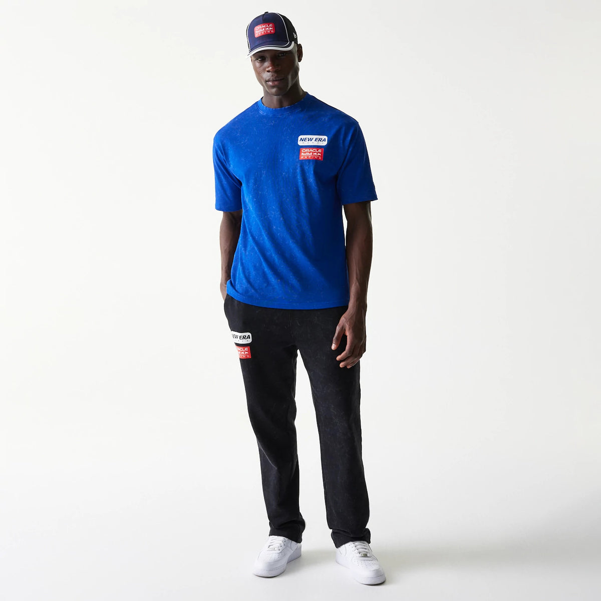 New Era Red Bull Racing Linear Graphic Blue Oversized T-Shirt, front view on-model with matching black trousers and cap, features a raised logo patch on the chest and right leg, and a matching red and white embroidered patch on the cap front.