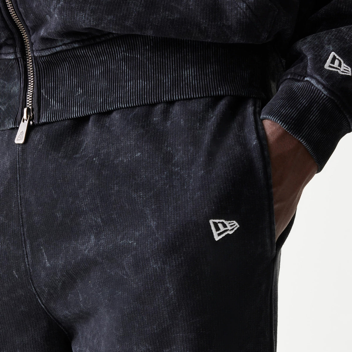New Era Red Bull Racing Straight Leg Black Straight Leg Joggers, close-up view showing white embroidered New Era flag logo on the left hip, with ribbed waistband and the model's hand in the pocket.