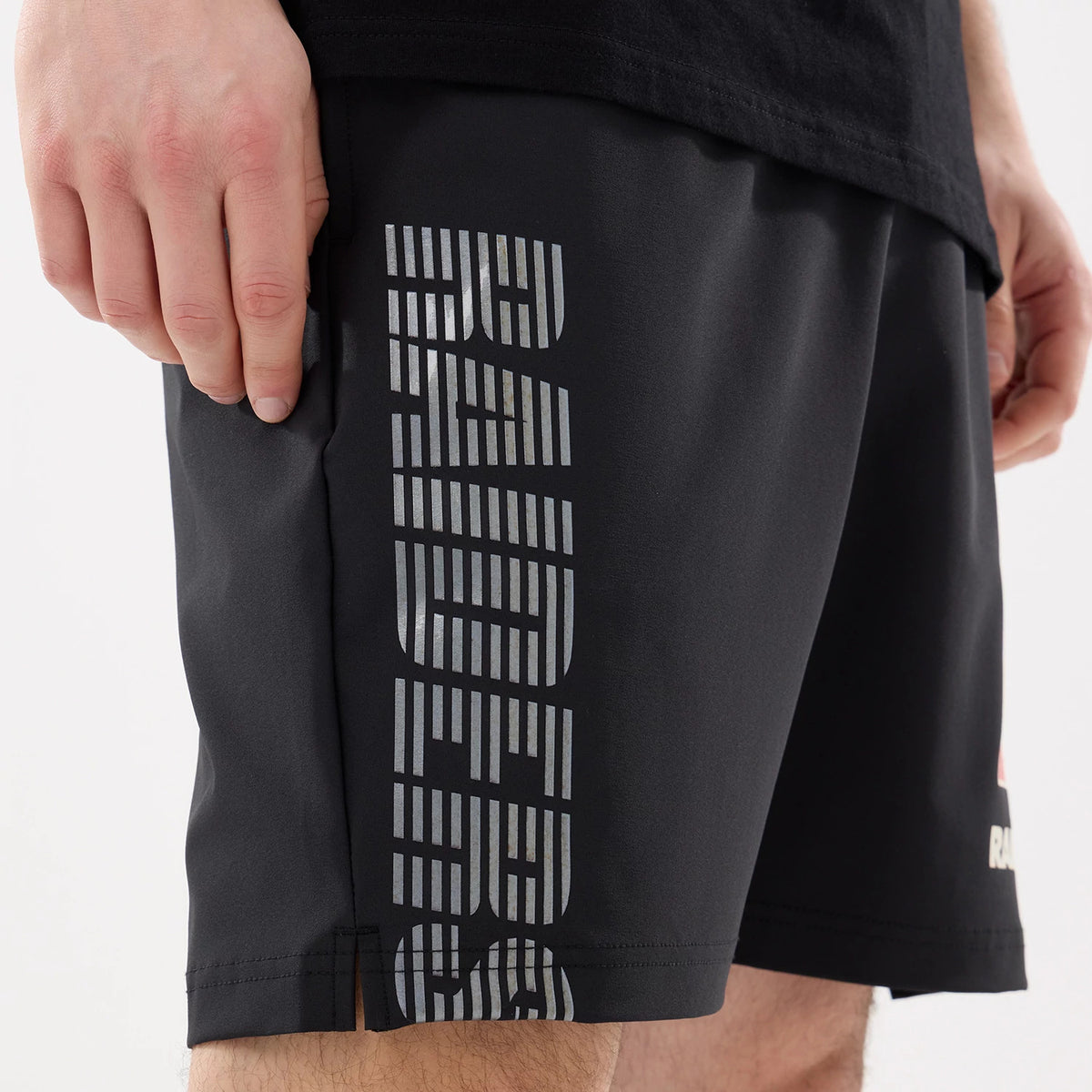 New Era Las Vegas Raiders NFL Match Black Oversized Shorts, side view showing the large silver vertical RAIDERS lettering on the right leg and a small embroidered logo near the hem, worn by a model with a black T-shirt.