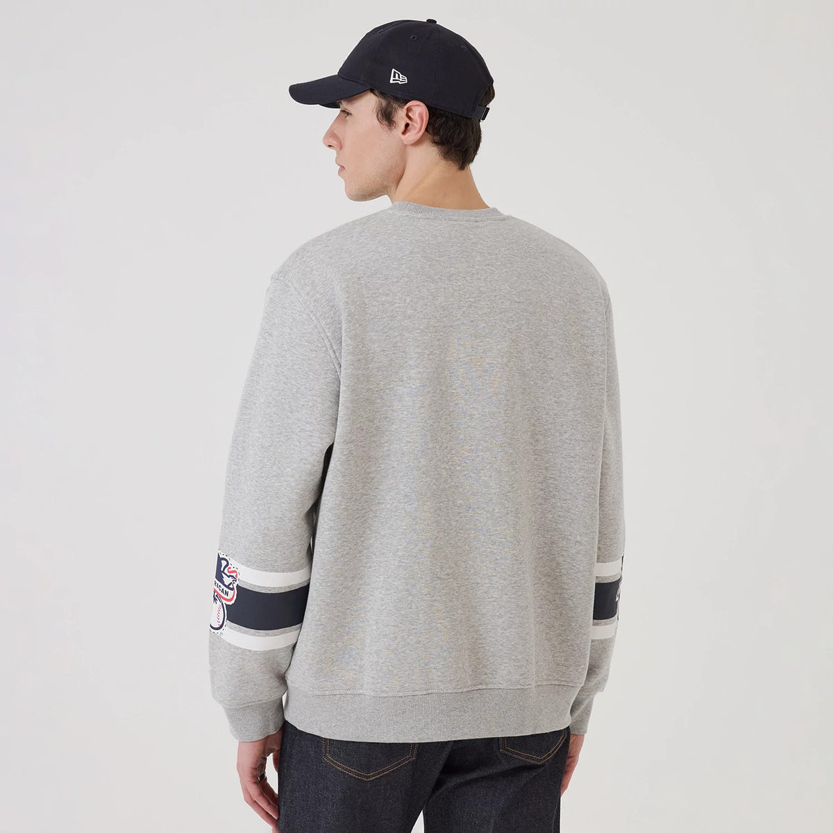 New Era New York Yankees MLB Sport Classic Grey Crew Neck Sweater, back view on a model wearing a matching cap, showing the grey fabric, long sleeves with navy and white stripes, and a relaxed fit.