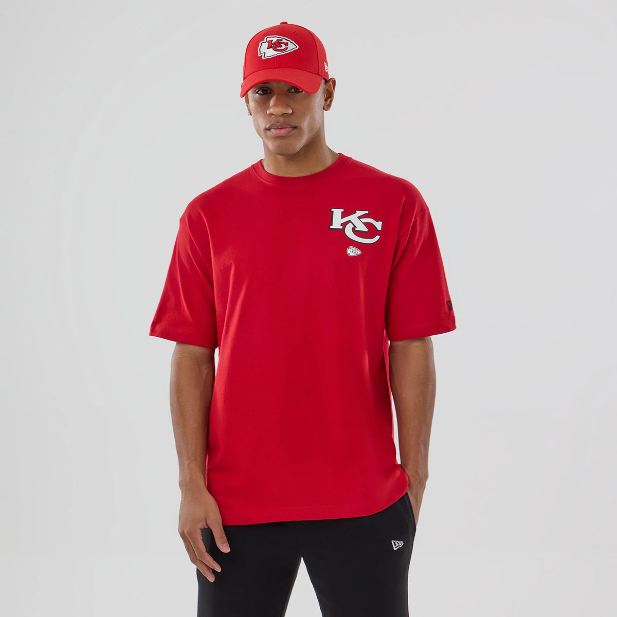 New Era Kansas City Chiefs NFL Graphic Red T-Shirt, front view on-model paired with a matching red cap, featuring an embroidered KC logo on the left chest and a small circular team logo beneath it.