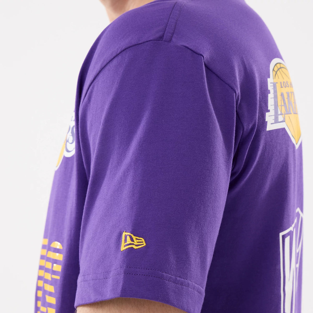New Era LA Lakers NBA Match Purple T-Shirt, side view showing a purple sleeve with a small yellow embroidered New Era logo near the cuff and a view of the Los Angeles Lakers graphic on the back.
