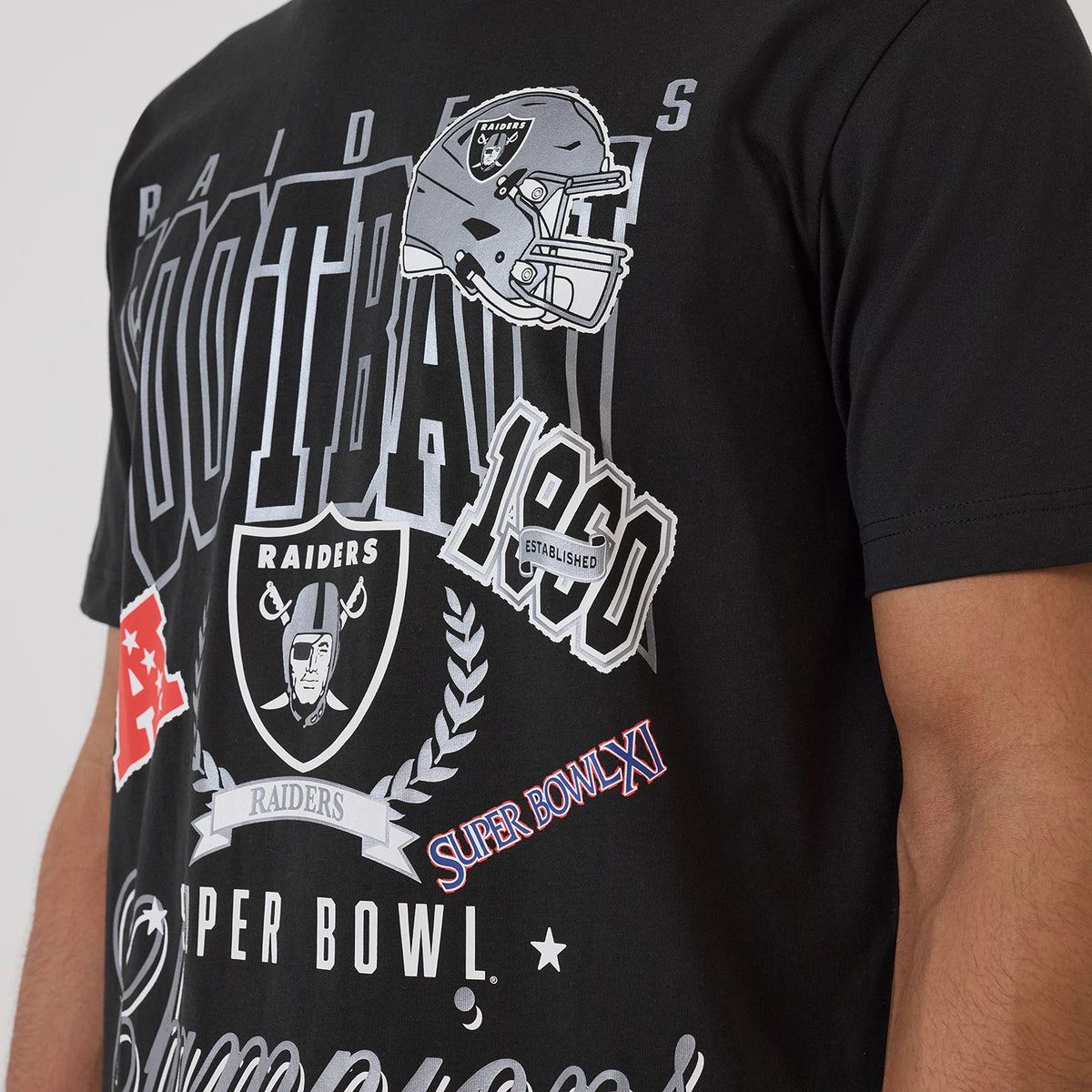 New Era Las Vegas Raiders NFL Sport Classic Black T-Shirt, front view on-model showing a large printed graphic with Raiders helmet, logo and lettering, championship symbols, and the word FOOTBALL spanning across the chest.