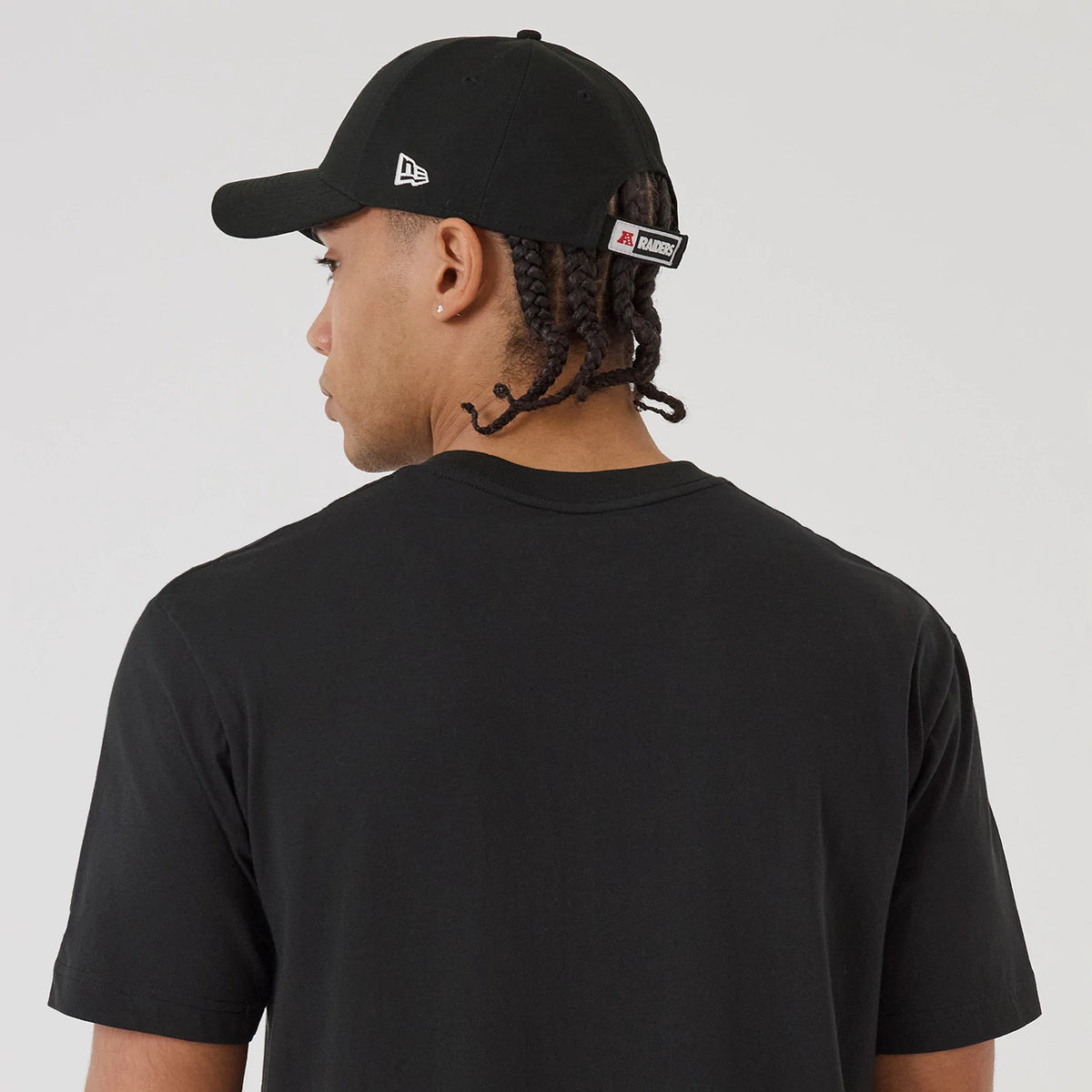 New Era Las Vegas Raiders NFL Sport Classic Black T-Shirt, back view on-model with a matching black cap, displaying the plain black back of the shirt and an embroidered New Era logo on the side of the cap.