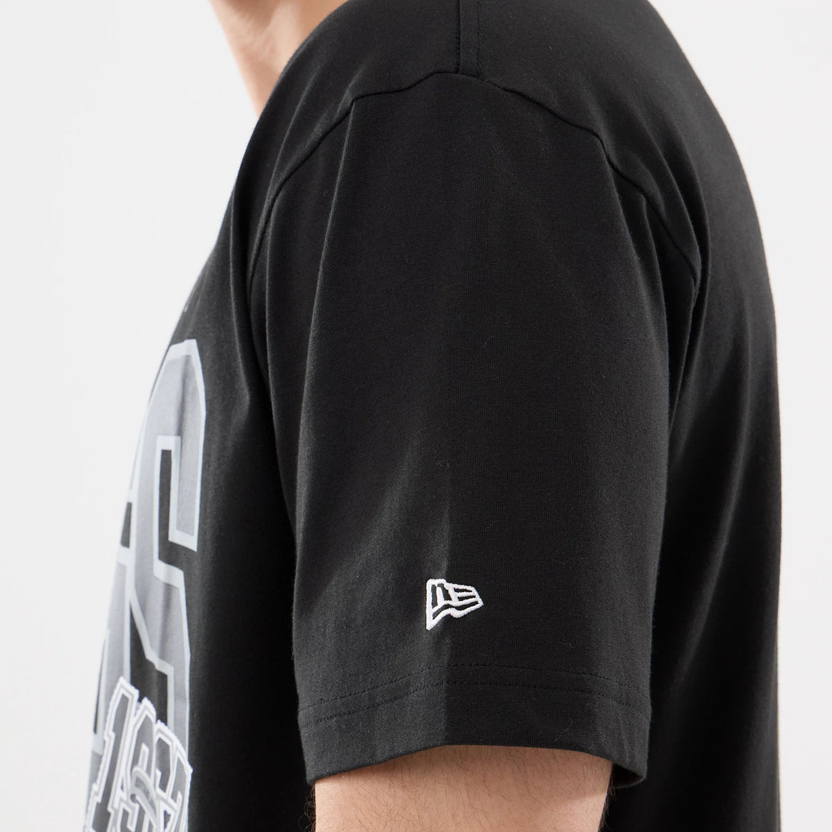 New Era LA Kings NHL Sport Classic Black T-Shirt, side view highlighting the short sleeve with a white embroidered New Era logo near the hem and grey printed lettering on the upper back.