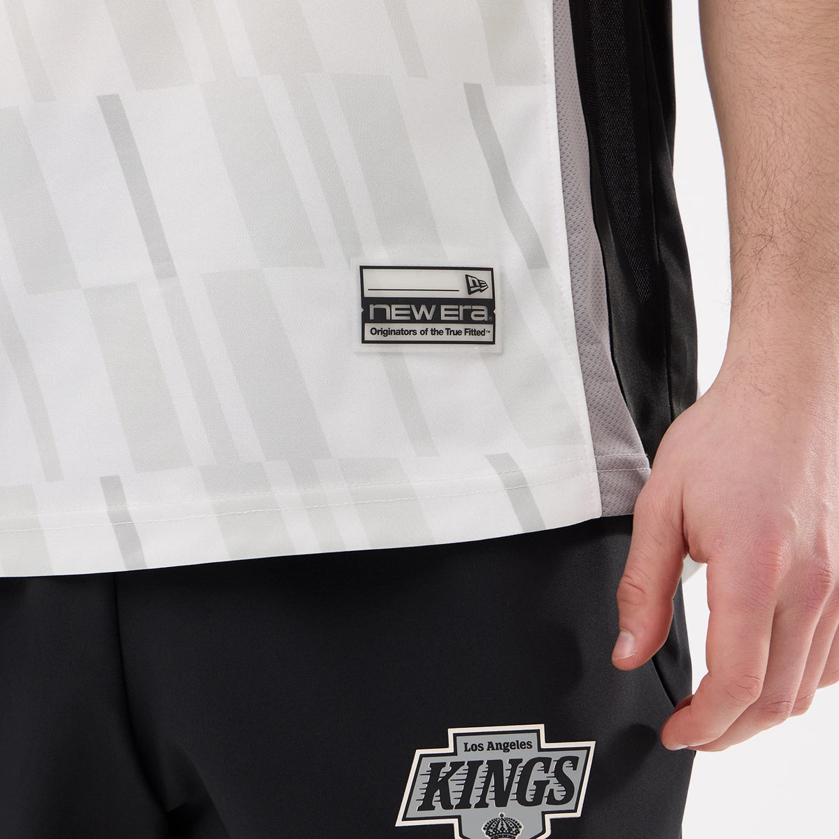 New Era LA Kings NHL Match Black T-Shirt, on-model view showing the lower half of the shirt with a New Era embroidered logo patch near the hem and a grey pattern, paired with trousers featuring the Kings logo.