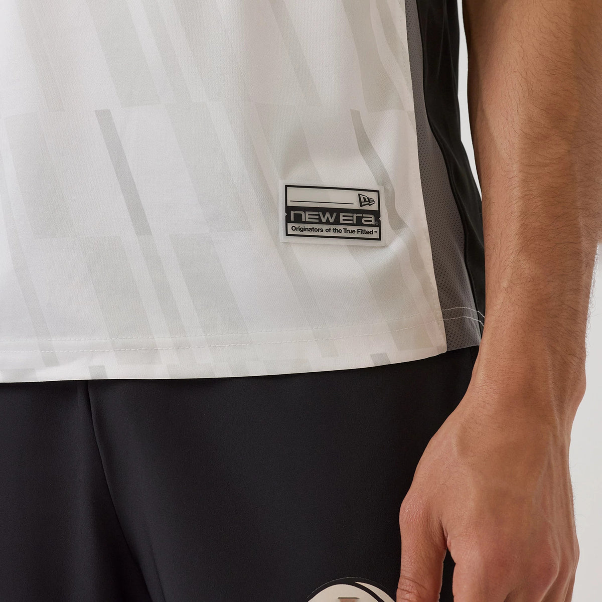 New Era Brooklyn Nets NBA Match Black T-Shirt, three-quarter view showing a black and white geometric pattern on the lower section, with an embroidered New Era logo label near the hem above black shorts.