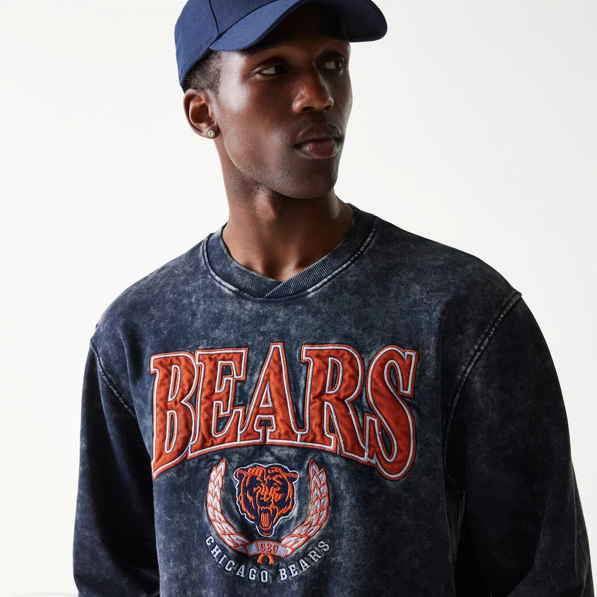 New Era Chicago Bears NFL Navy Crew Neck Sweater, front view on a model wearing a navy cap, featuring large orange Bears text and logo embroidery across the chest on a distressed navy fabric.