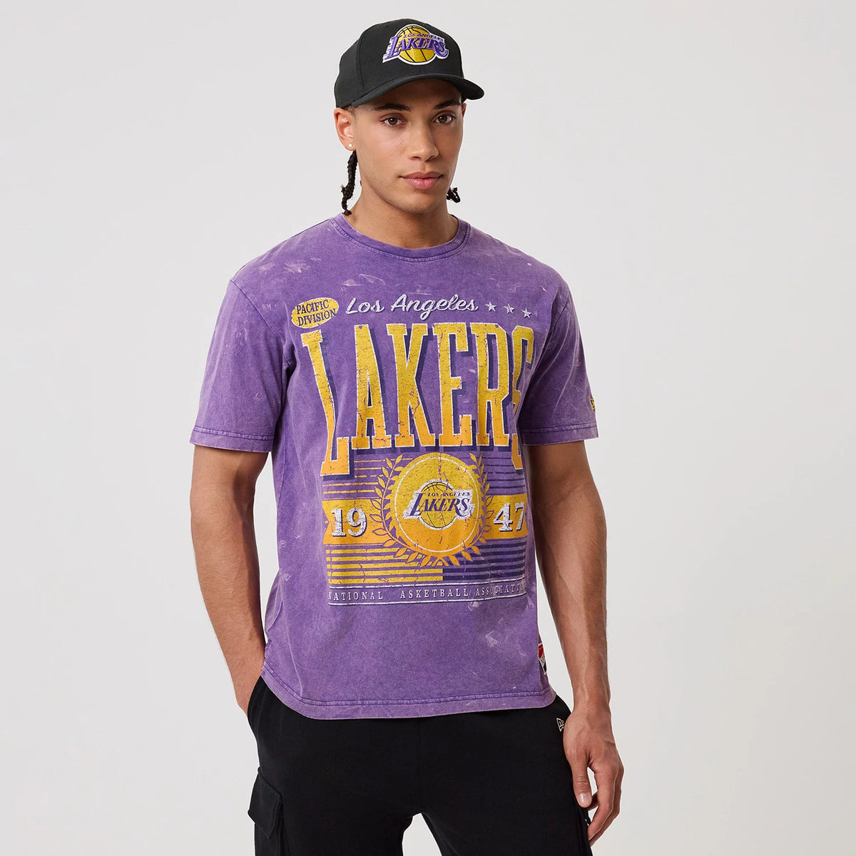 New Era LA Lakers NBA Purple T-Shirt, front view on-model featuring yellow Lakers lettering and graphic design across the chest, Los Angeles text above, and a small embroidered logo on the sleeve.