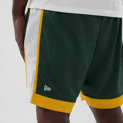 New Era Athletics MLB Dark Green Mesh Shorts, on-model front view showing a white panel with yellow trim on the sides, dark green mesh fabric, and an embroidered New Era logo above the yellow hem at the left leg.