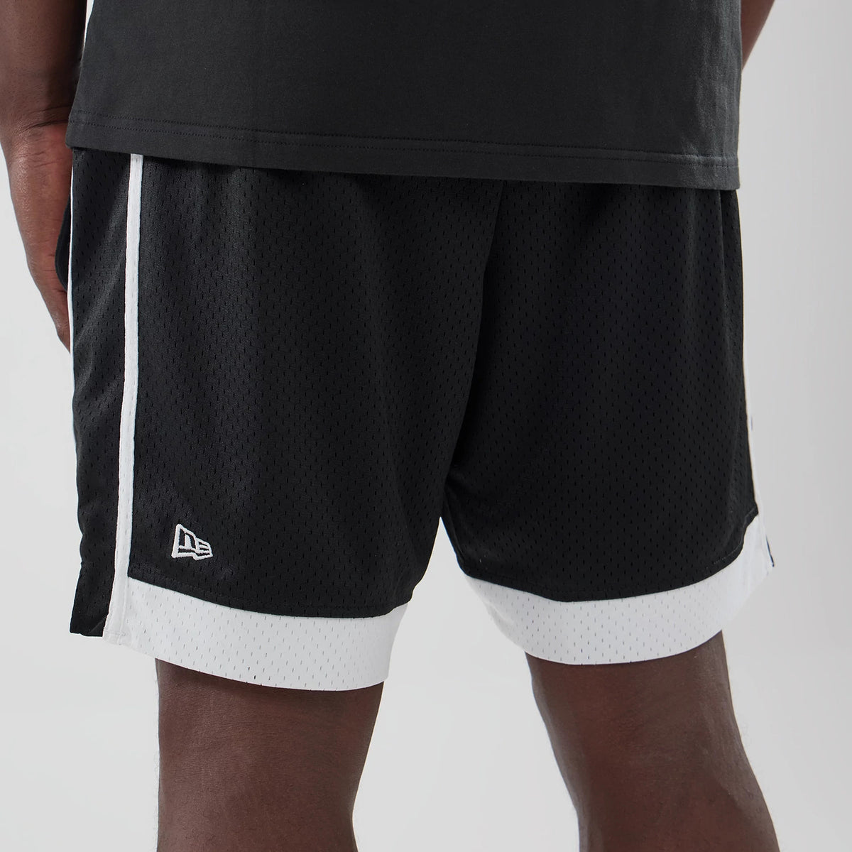 New Era LA Dodgers MLB Black Mesh Shorts, on-model view showing the black mesh fabric with white side stripes and white trim at the hem, featuring an embroidered New Era logo near the left leg opening.