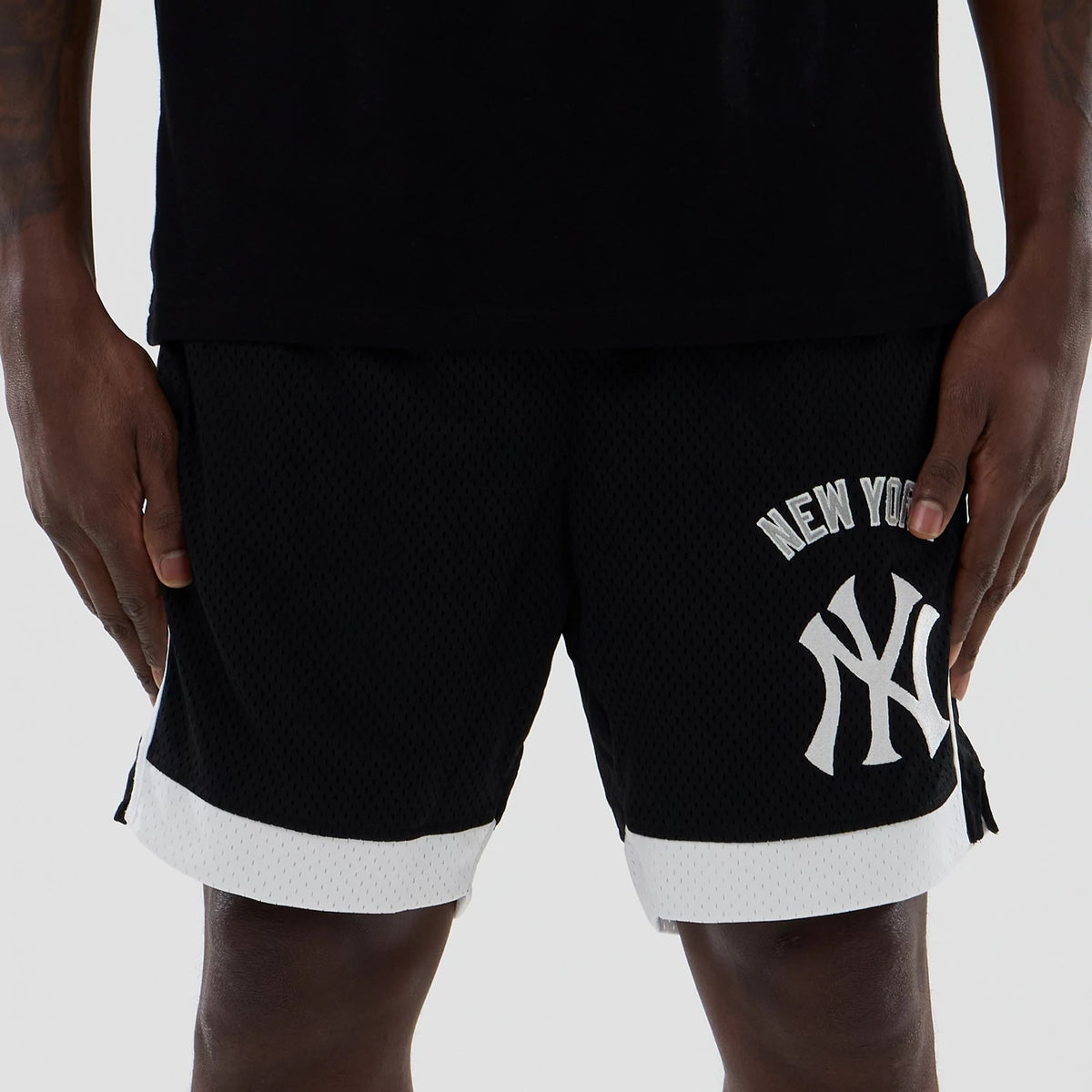 New Era New York Yankees MLB Black Mesh Shorts, front view showing white embroidered New York Yankees lettering and logo on the left leg, with contrasting white trim at the hem and side slits, styled on a model.
