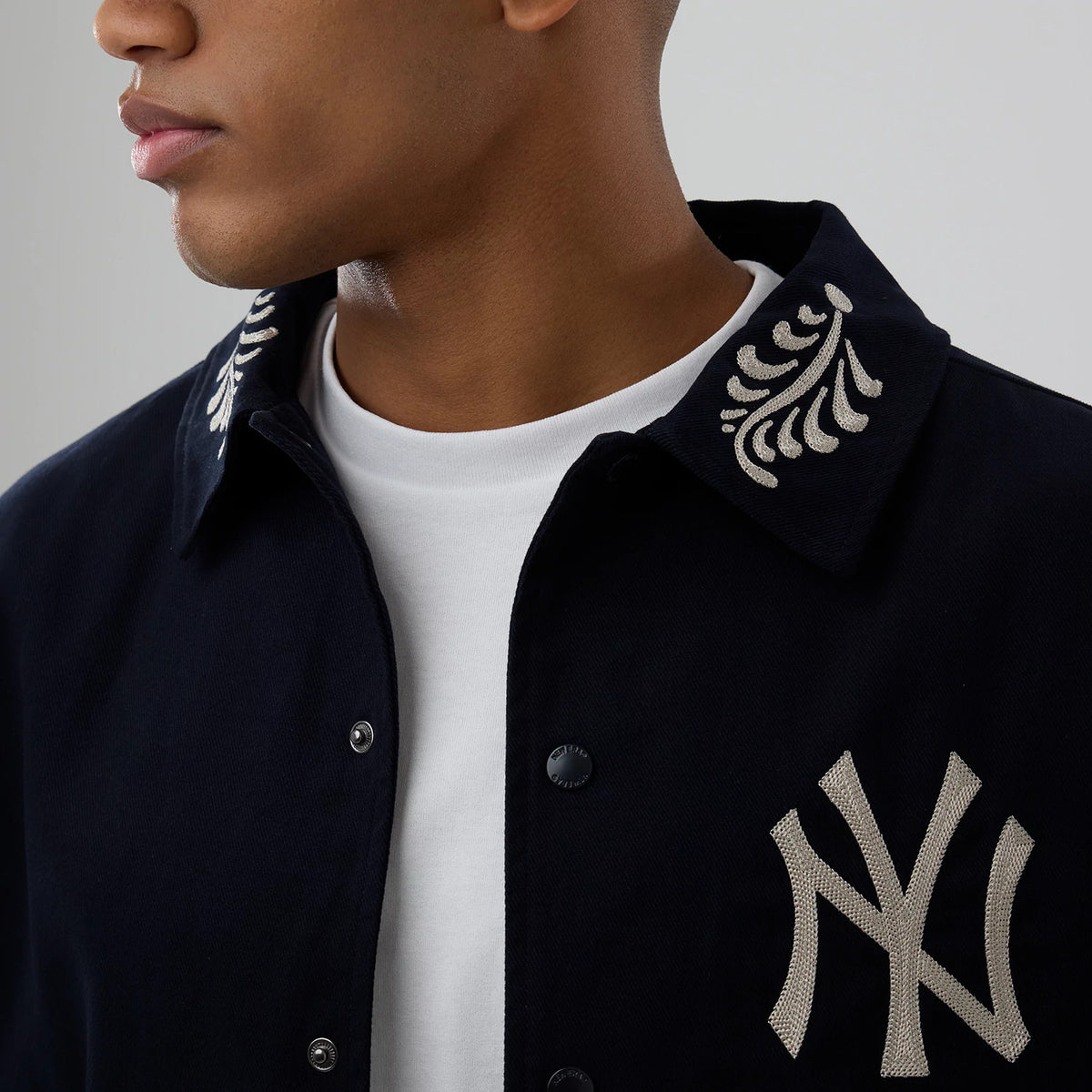 New Era New York Yankees MLB Script Navy Coach Jacket, front view on-model displaying embroidered silver logo on the left chest and decorative silver embroidery on the collar, button fastening down the centre over a plain white t-shirt underneath.