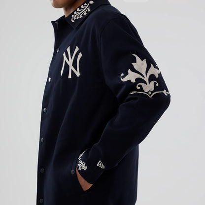 New Era New York Yankees MLB Script Navy Coach Jacket, three-quarter view showing the white embroidered NY logo on the chest, intricate white designs on the sleeves and collar, and the embroidered New Era logo on the left cuff.